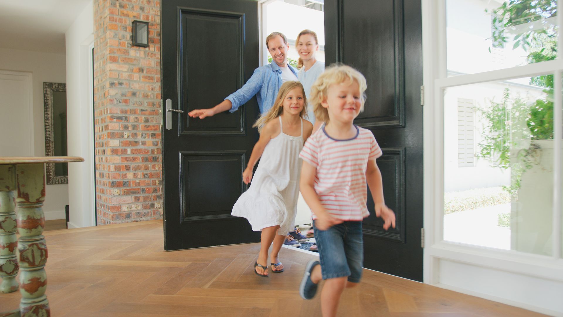 Family entering a bright home through the front door, with a young child running ahead.