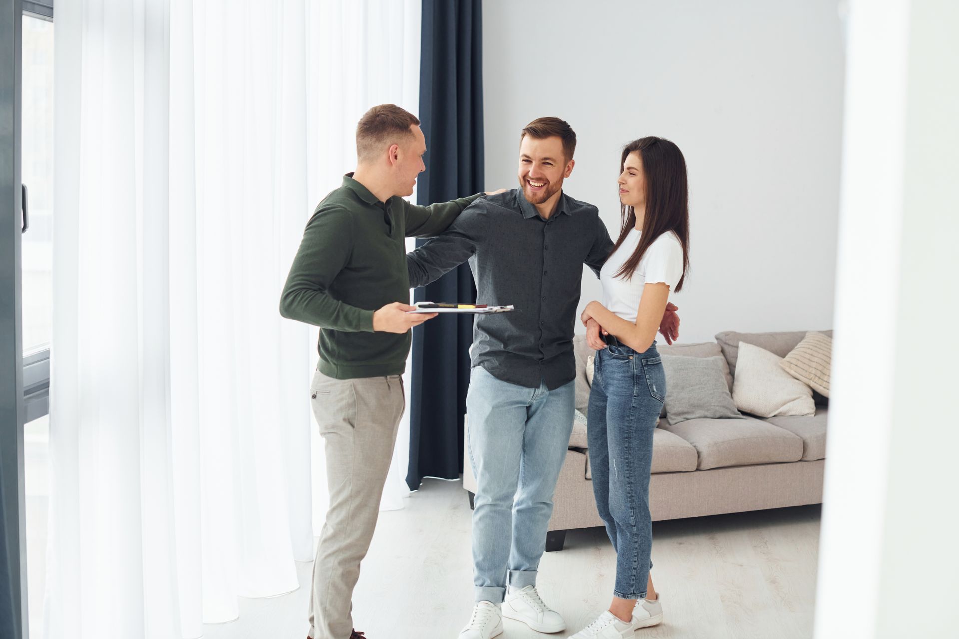 Three people discussing a house in a bright living room, with one holding a clipboard.