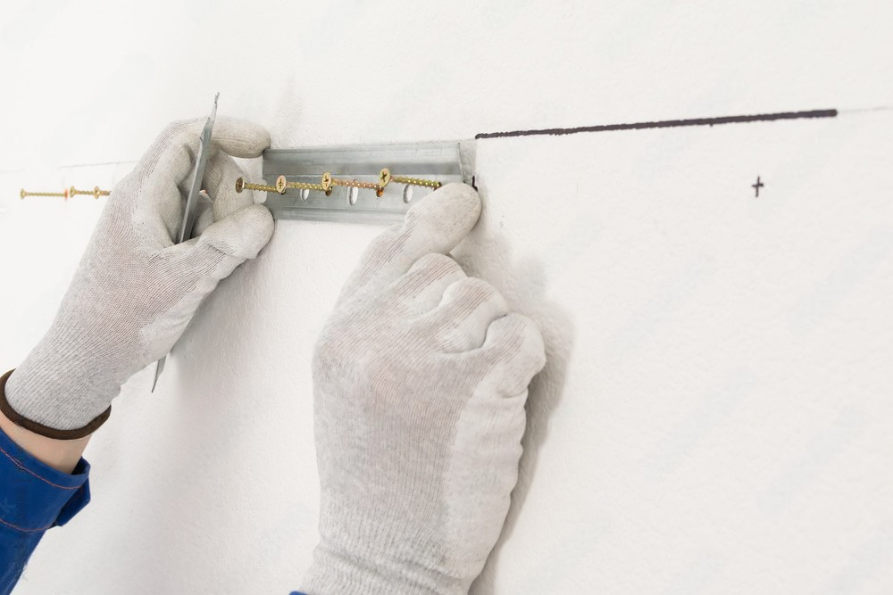 a person wearing white gloves is holding a metal bracket on a wall .