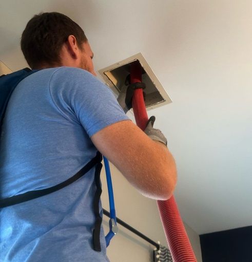 A man in a blue shirt is using a red hose to clean a vent