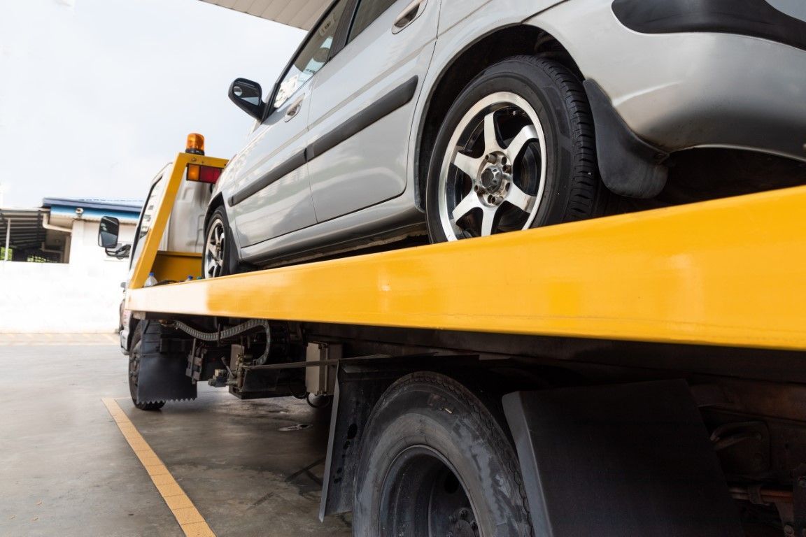 A car is being towed by a tow truck in a parking lot.
