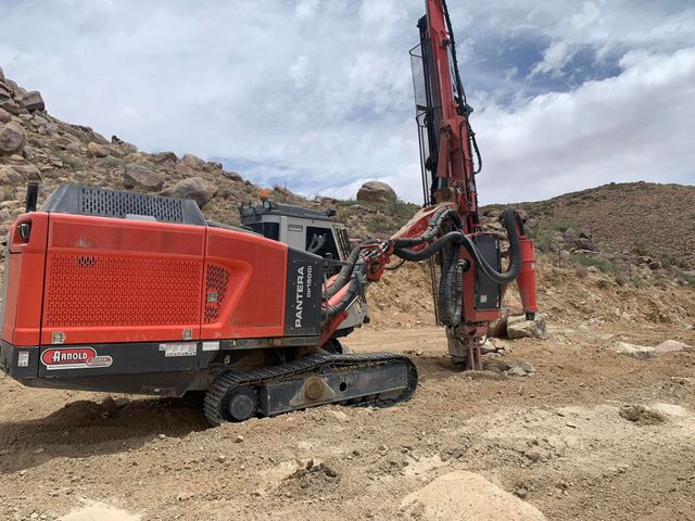 Red excavator drilling in a rocky construction site under a cloudy sky