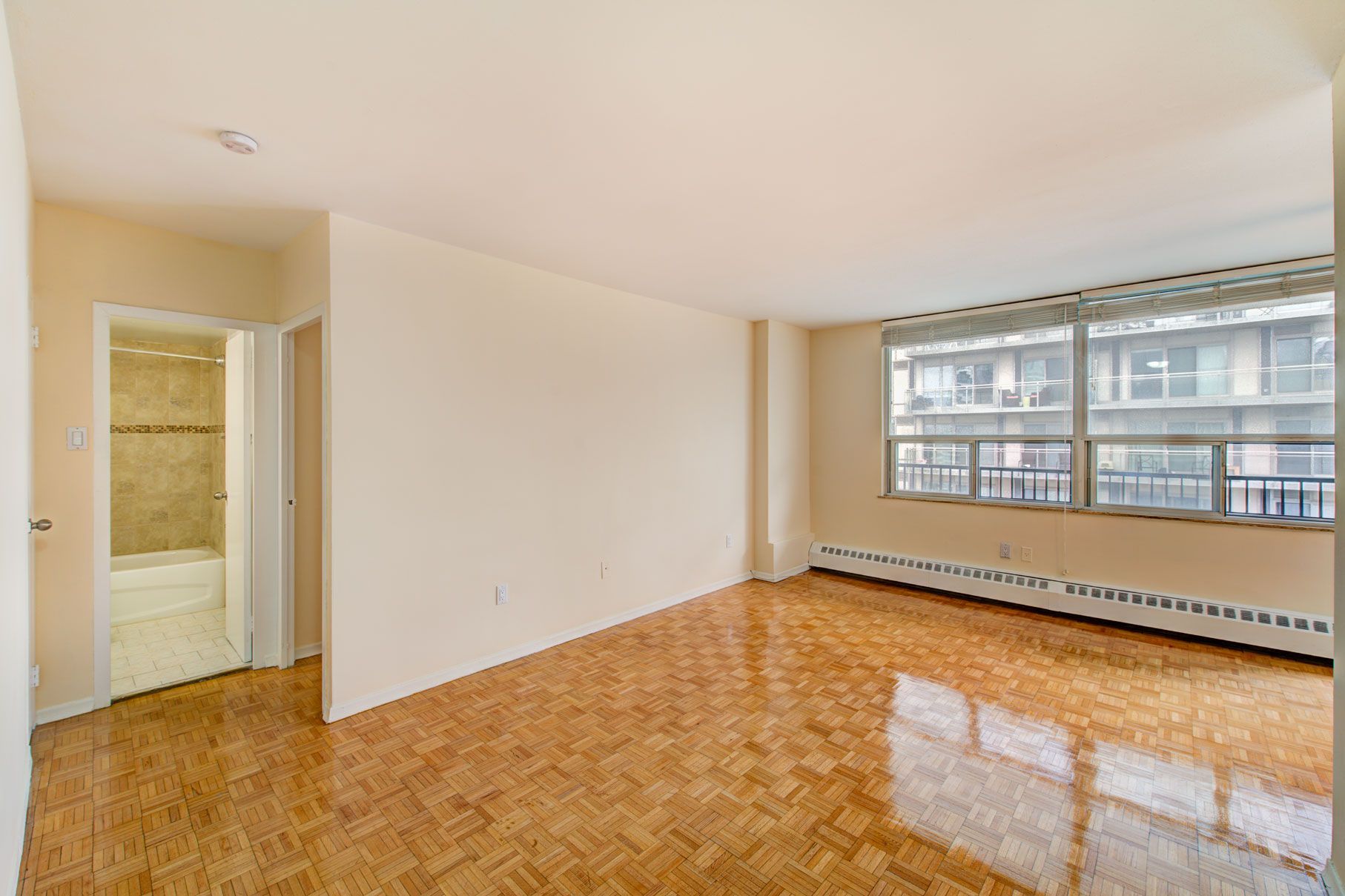 An empty living room with hardwood floors and a large window.