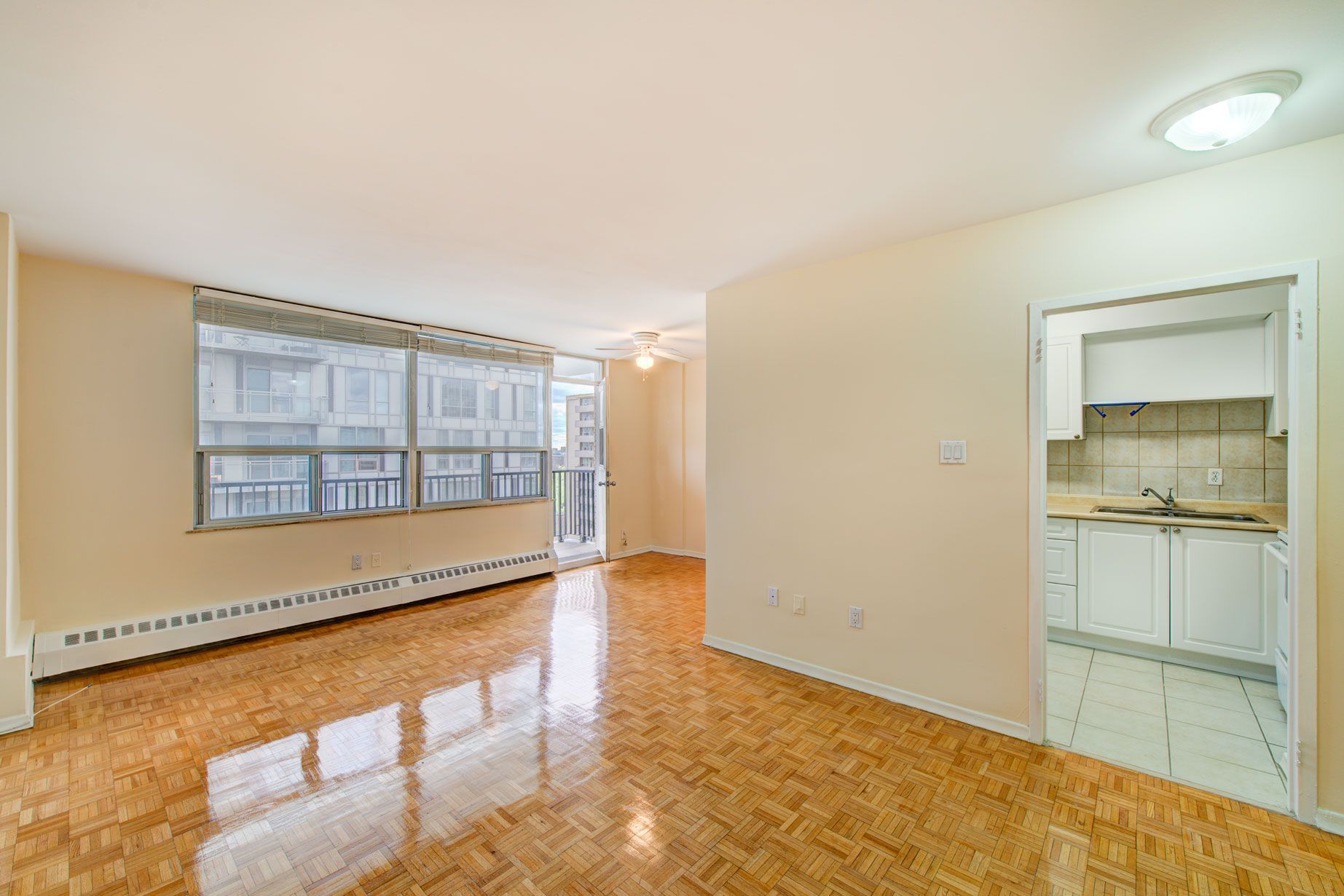 An empty living room with hardwood floors and a kitchen in the background.