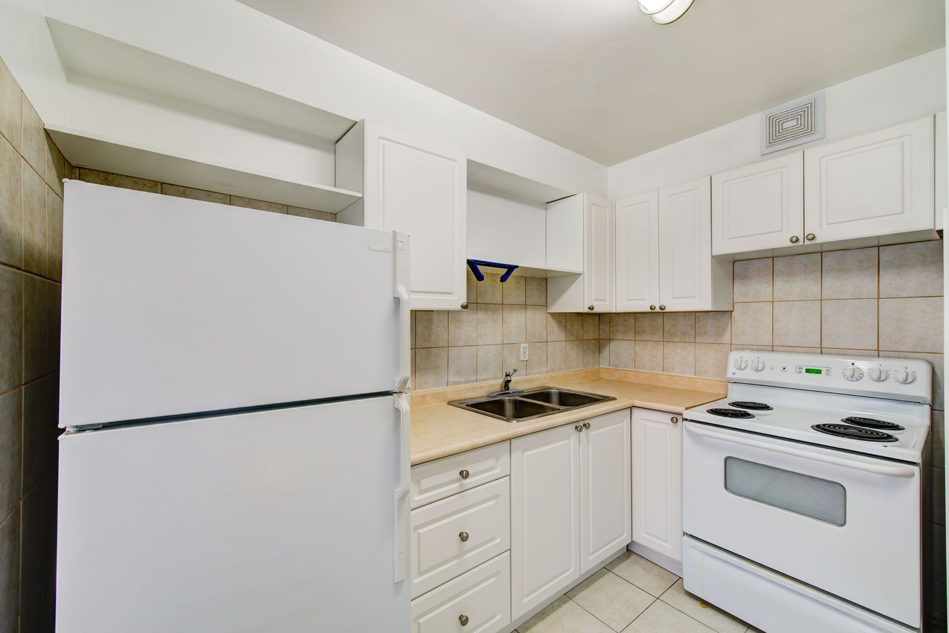 A kitchen with white cabinets , a refrigerator , a stove , and a sink.