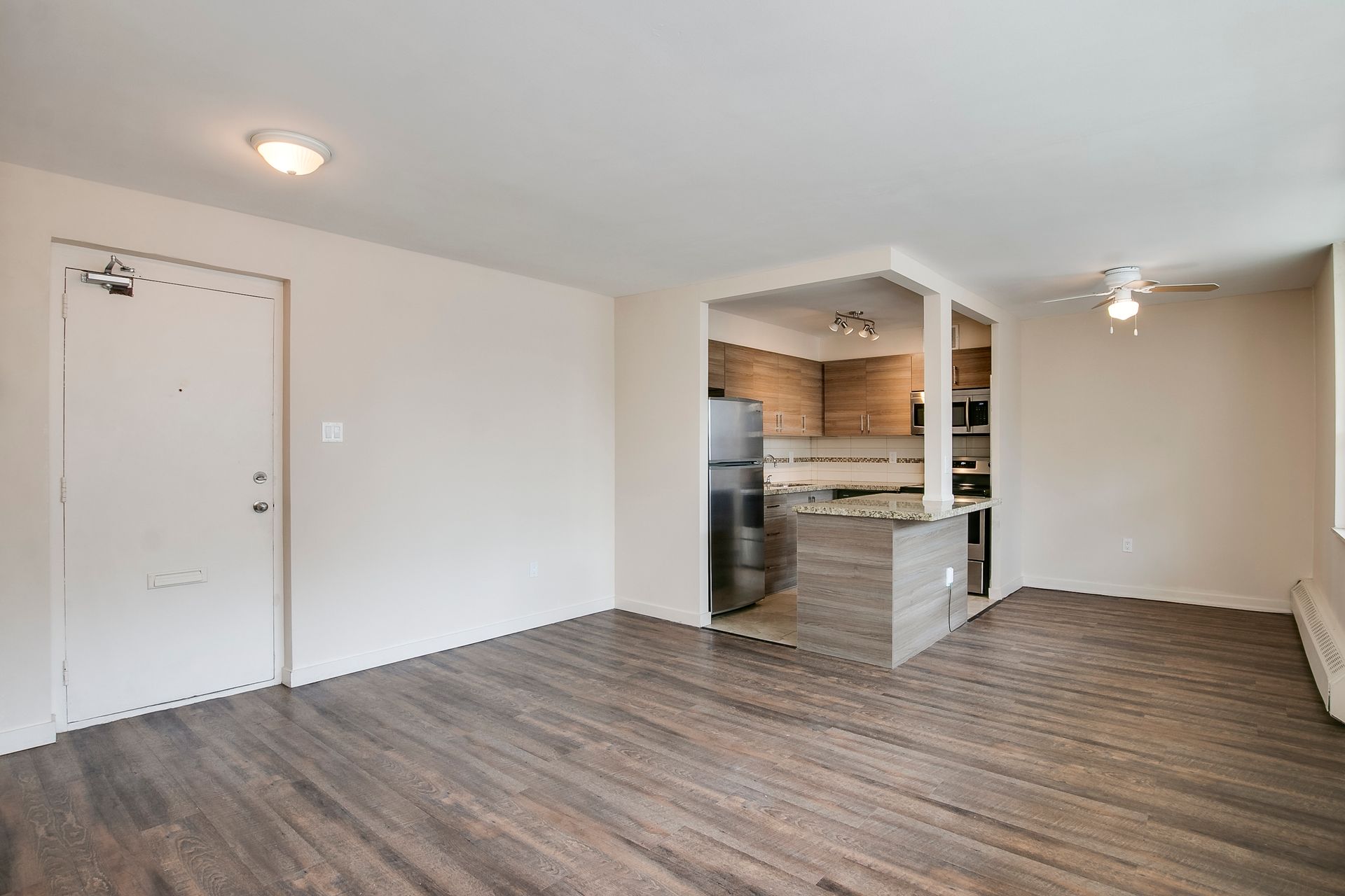 A living room with hardwood floors and a kitchen in the background.