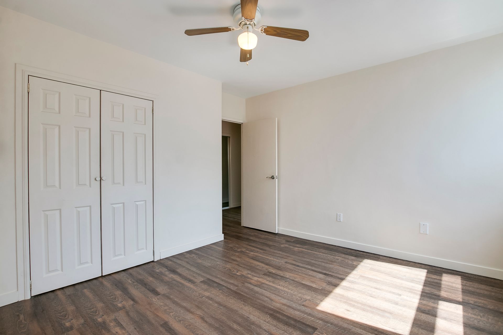 An empty bedroom with hardwood floors and a ceiling fan.