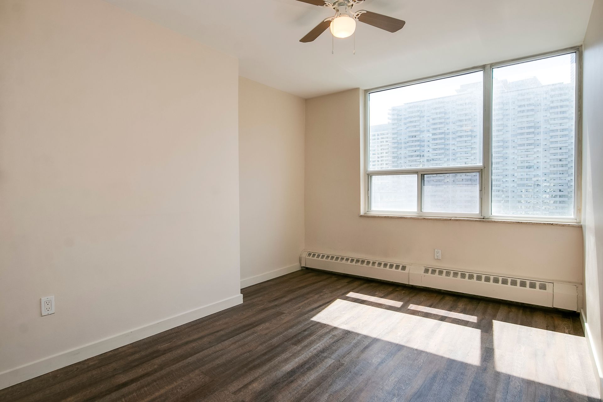 An empty room with a ceiling fan and a large window.