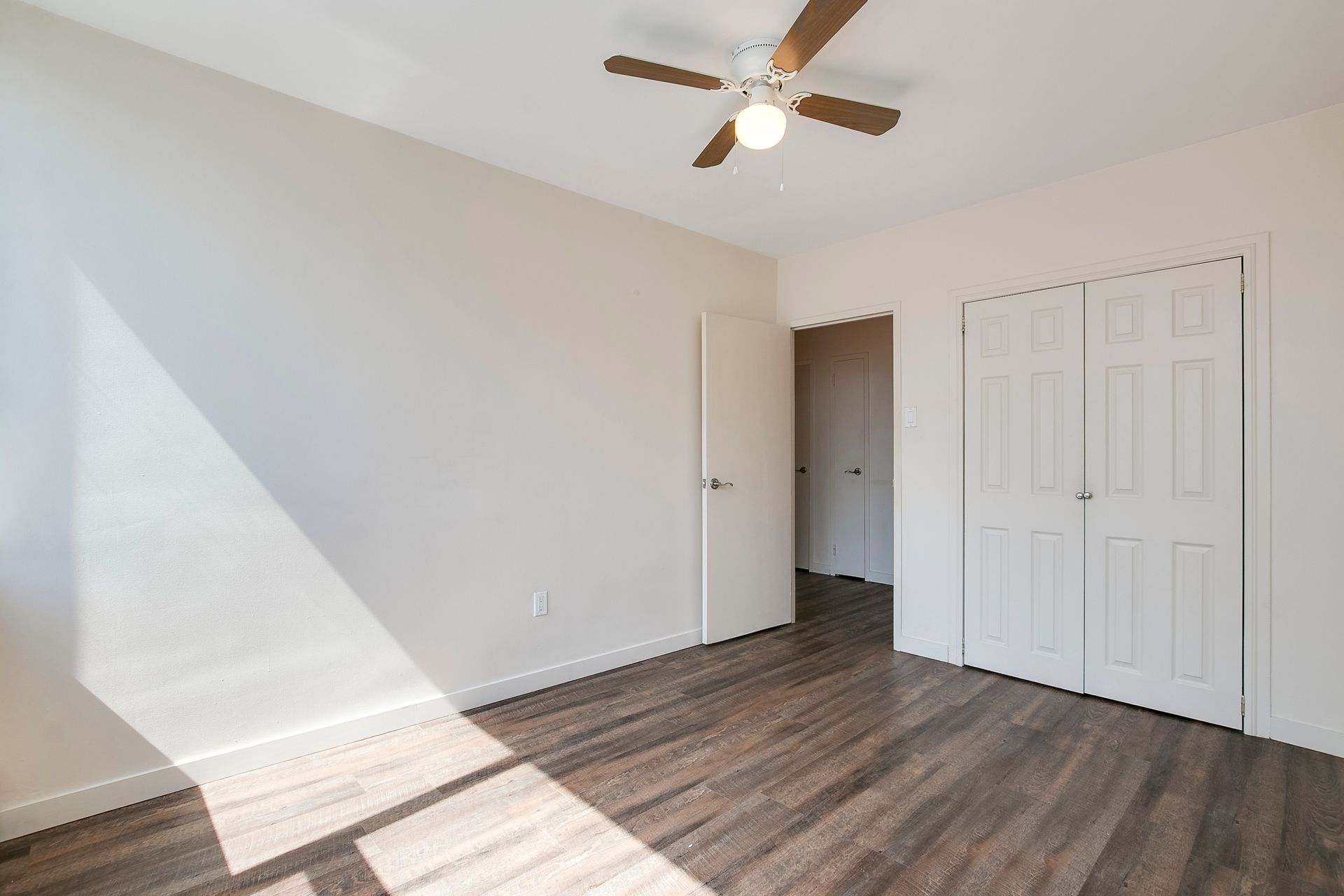 An empty bedroom with hardwood floors and a ceiling fan.