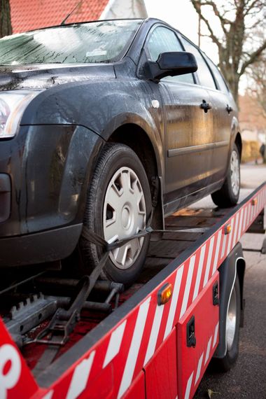 A black car is being towed by a tow truck.