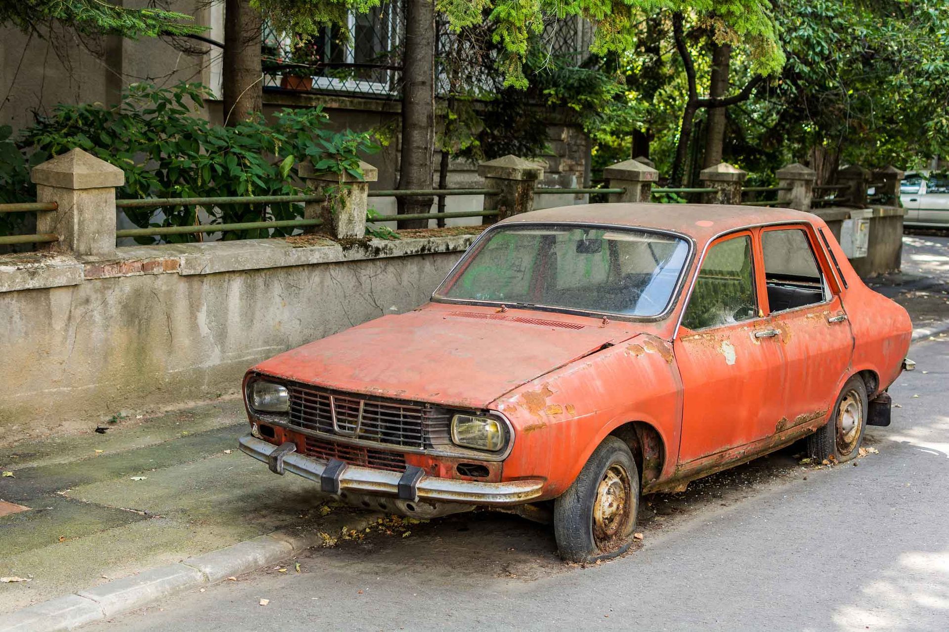 An old rusty red car is parked on the side of the road.