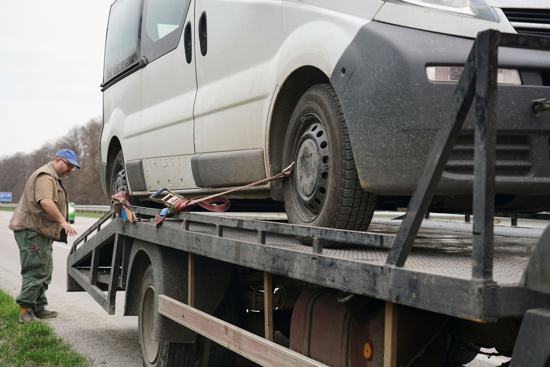 A man is standing next to a tow truck with a van on it.