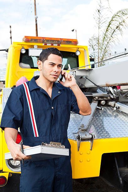 A man is talking on a cell phone in front of a tow truck.