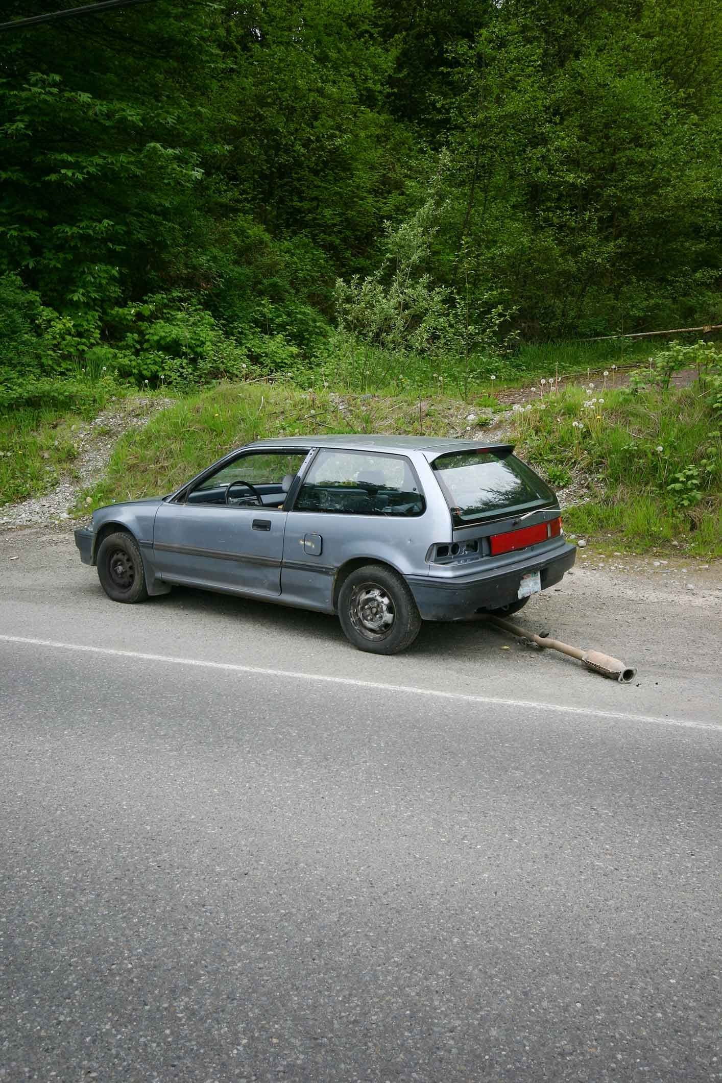 A car is parked on the side of the road next to a forest.