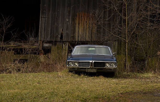 A blue car is parked in front of a wooden barn.