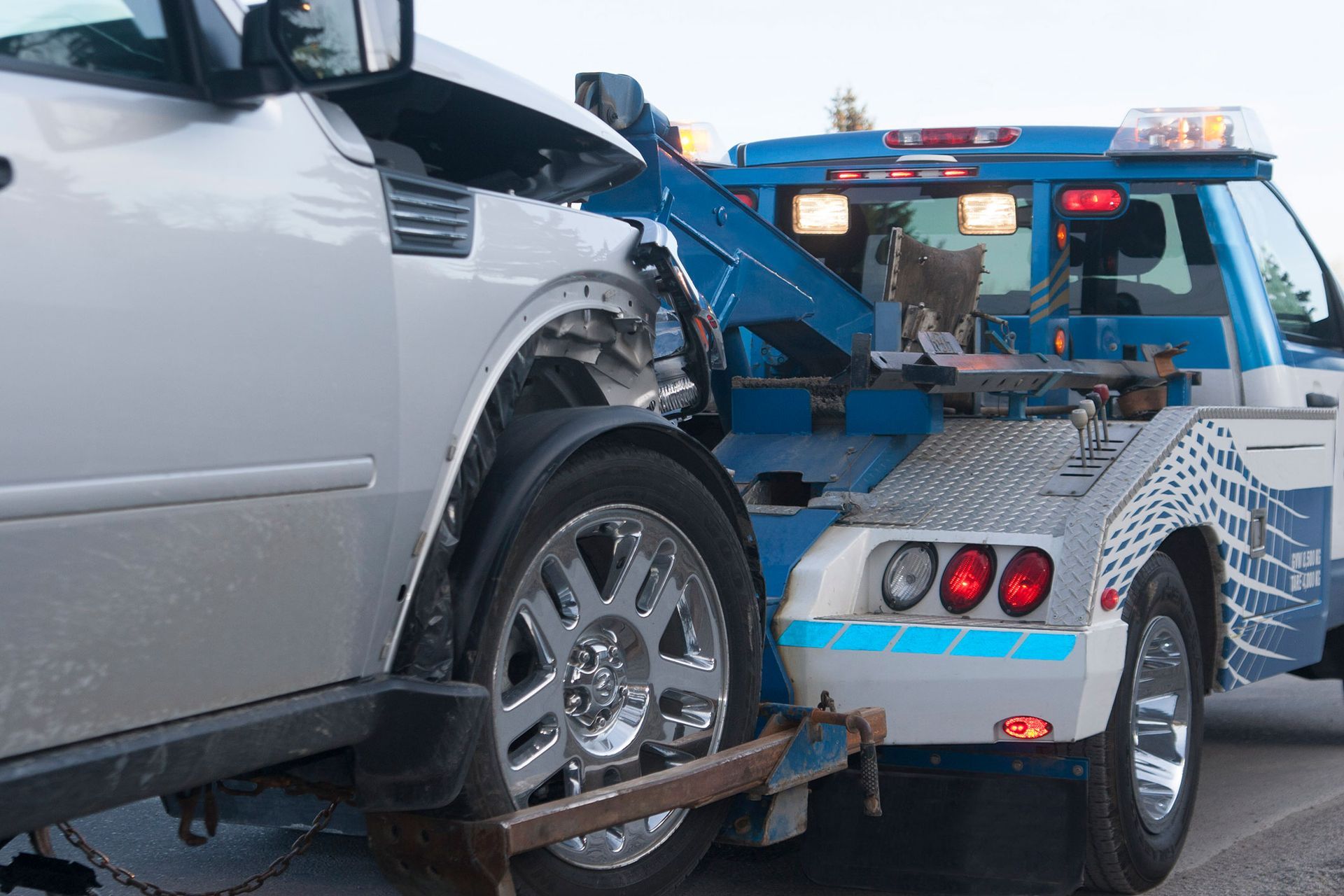 A silver car is being towed by a blue tow truck.