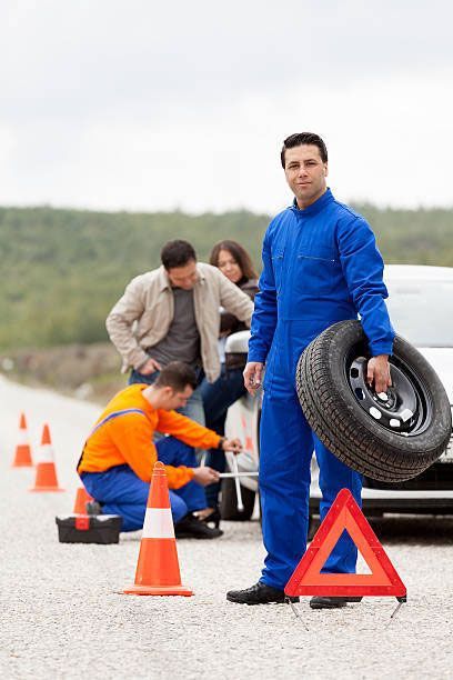 A man is holding a tire in front of a group of people changing a tire on a car.