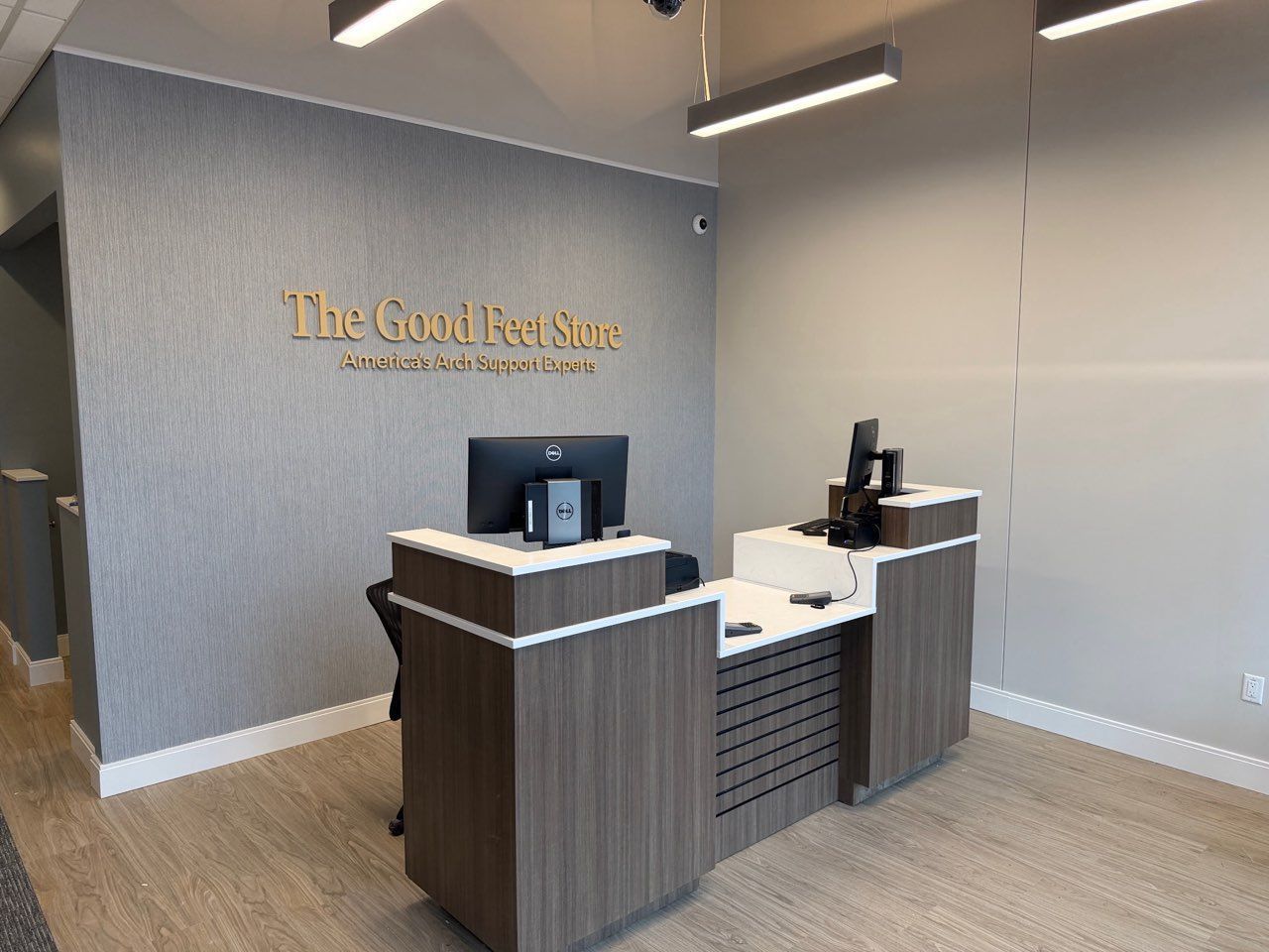 Reception desk with a computer inside The Good Feet Store, featuring gold lettering on a textured gray wall.