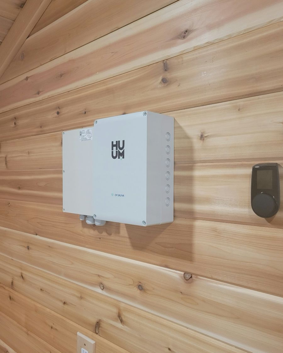 White Hummi inverter box mounted on wood paneling, with a small thermostat to the right.