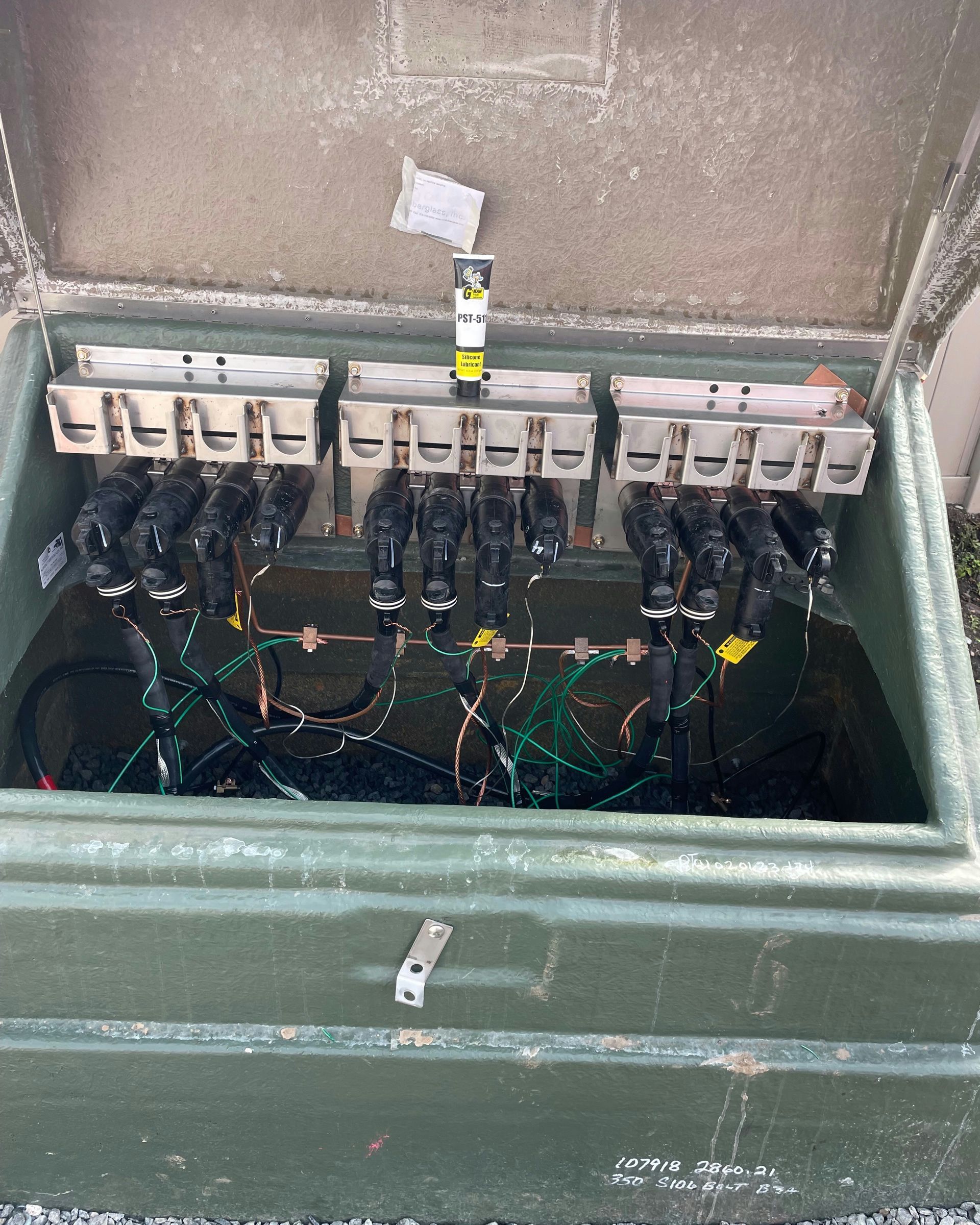 Open green electrical box with black cables, fuses, and wiring.