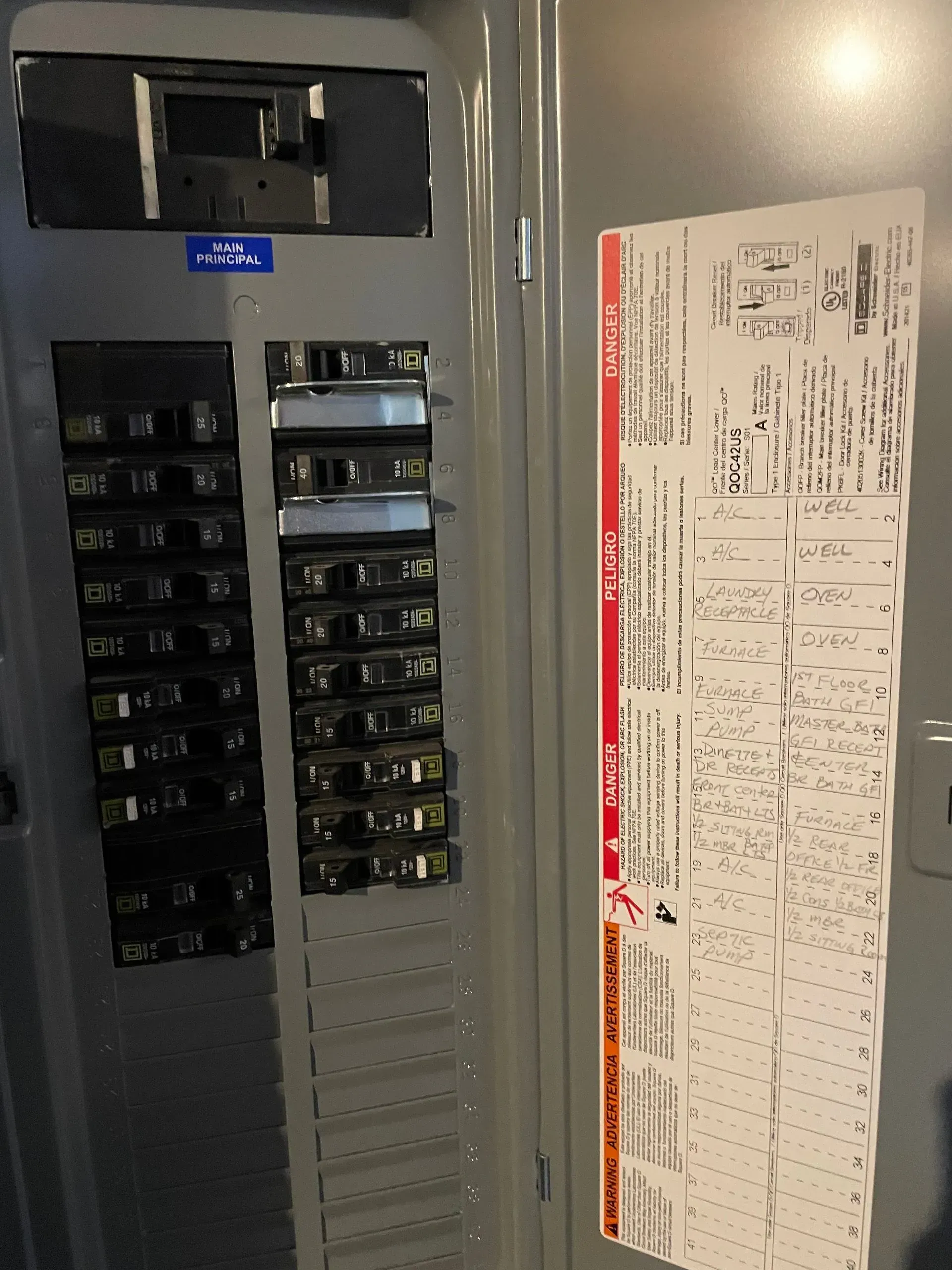 An indoor grey electrical breaker panel with a list of circuits on the right side and multiple switches on the left.