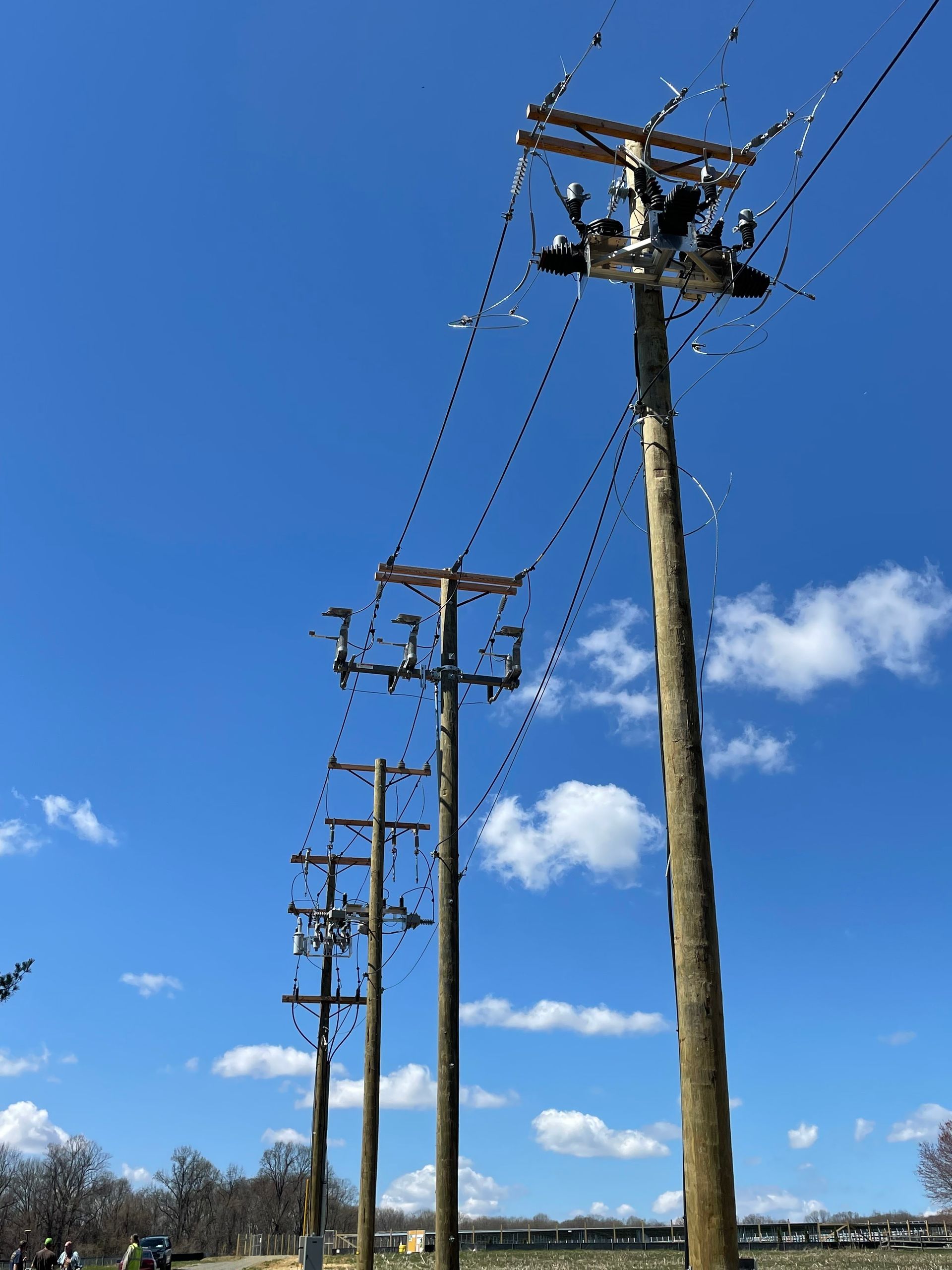 Wooden power poles with connected wires against a blue sky with clouds.