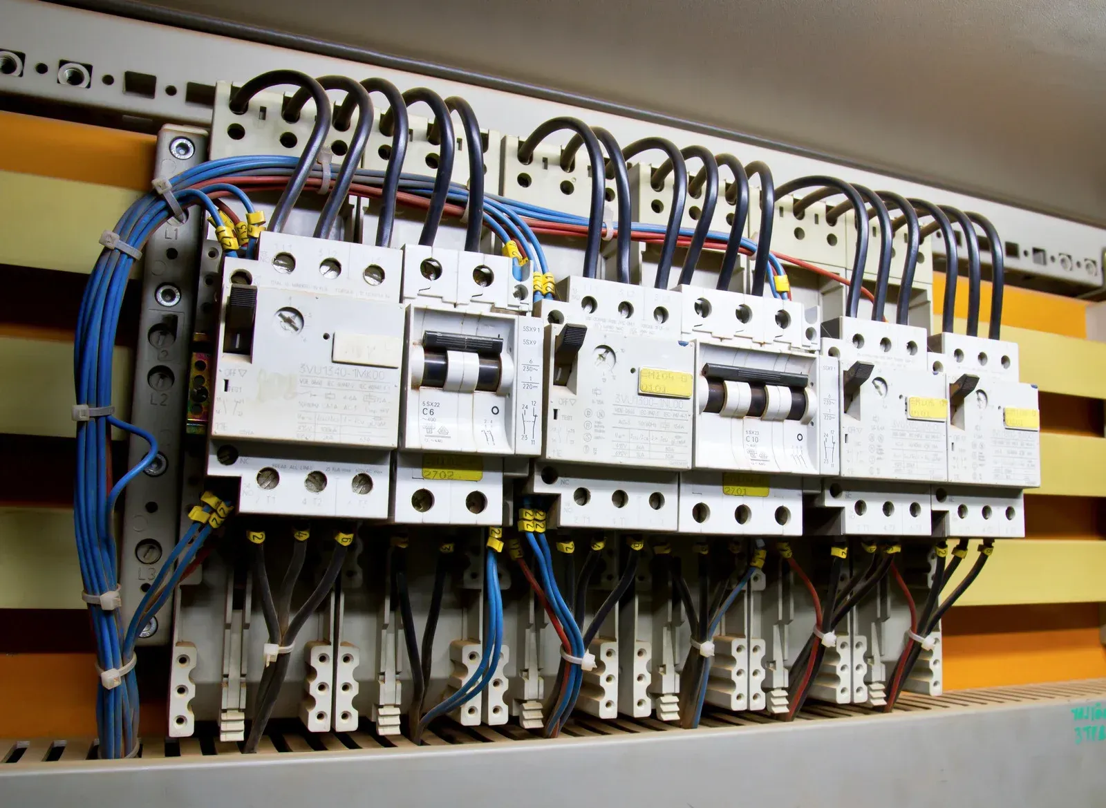 Electrical distribution panel with multiple white circuit breakers mounted on yellow bus bars and connected by blue wiring.