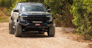 A black truck is driving down a dirt road.