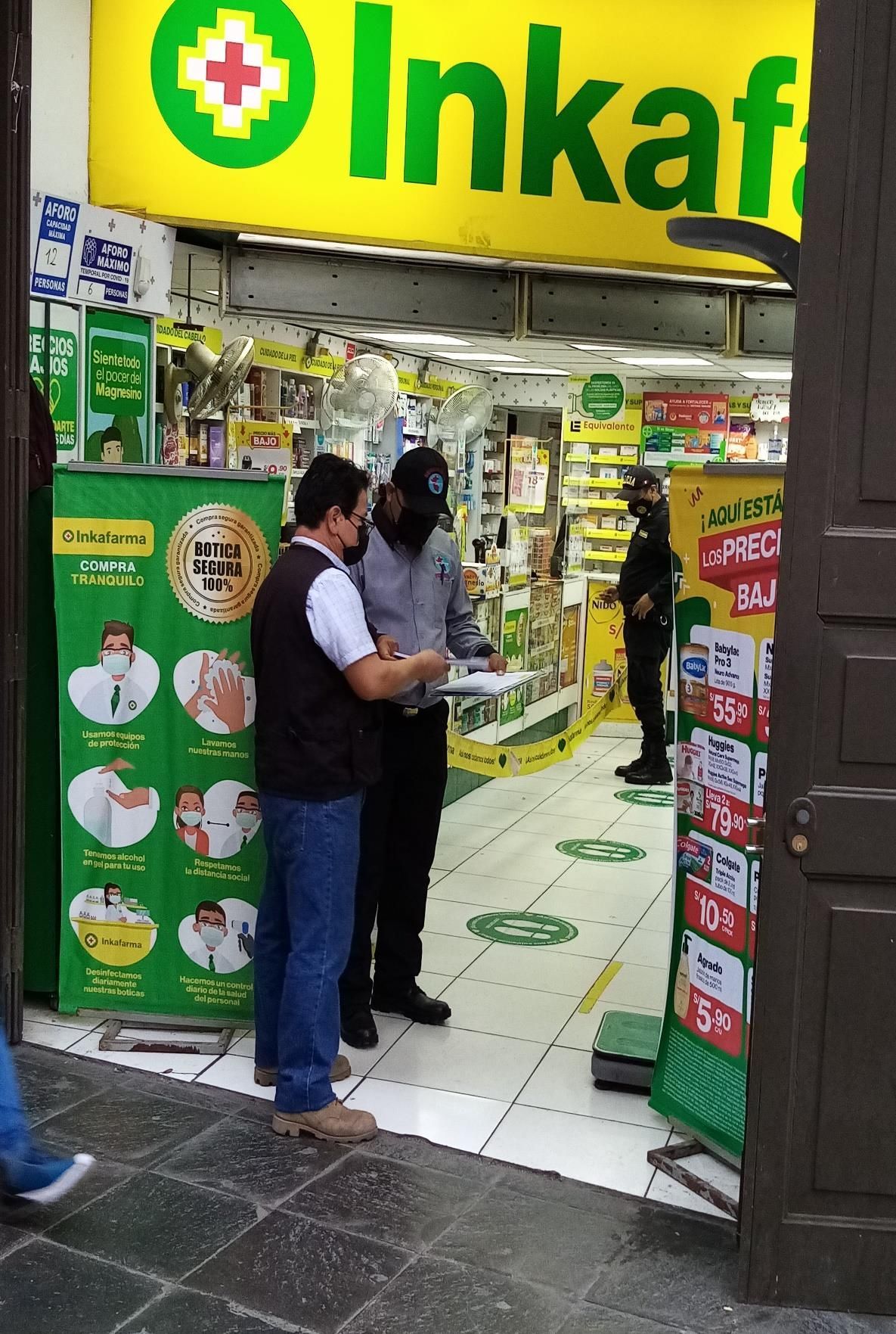 Dos hombres frente a una farmacia Inkafarma, uno de ellos con mascarilla. 
