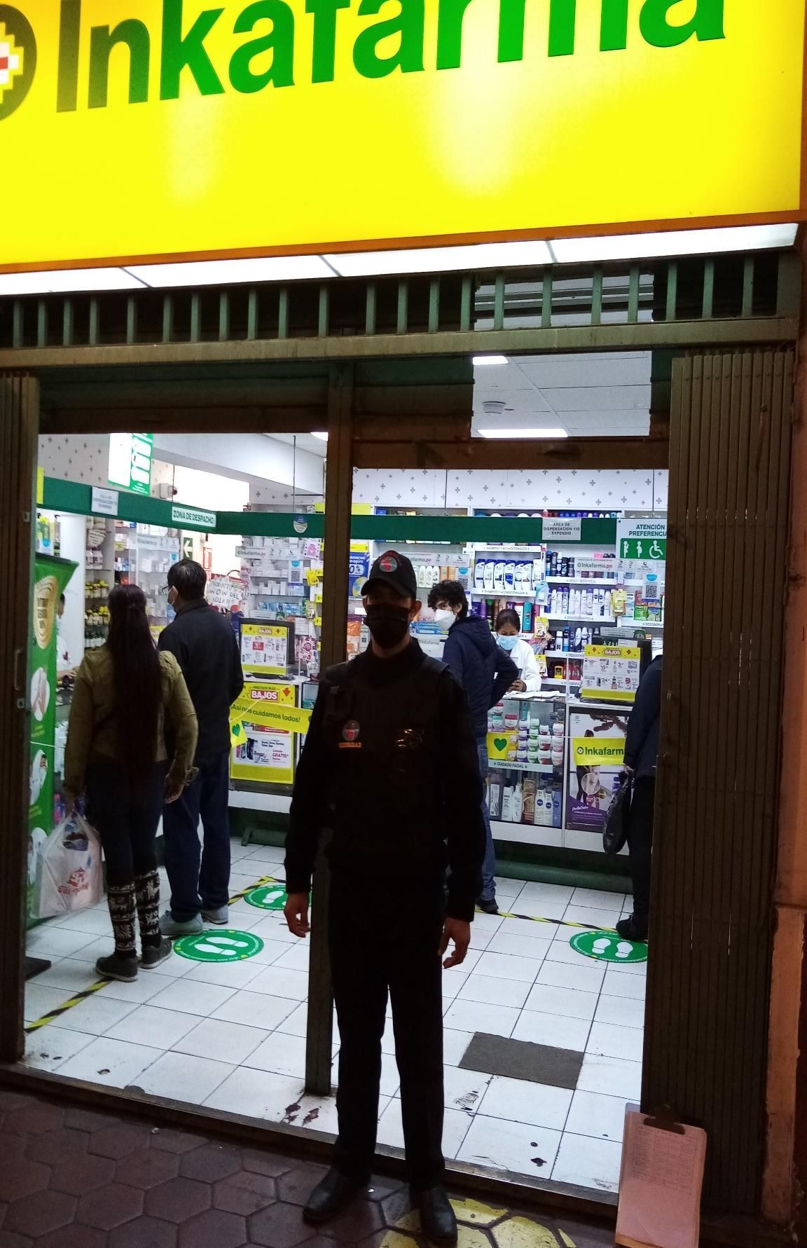 Un guardia de seguridad se encuentra frente a una farmacia Inkafarma con clientes dentro.