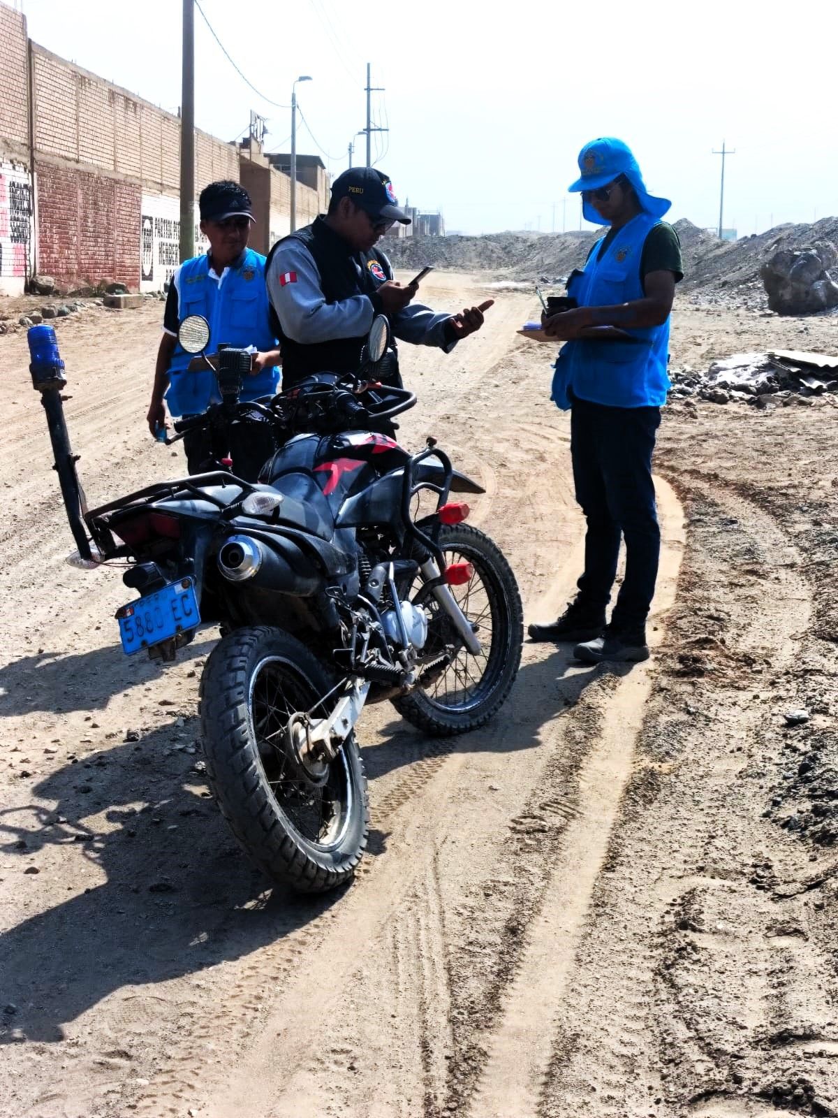 Agentes de policía cerca de una motocicleta en un camino de tierra; uno toma notas. Otros dos llevan chalecos azules.