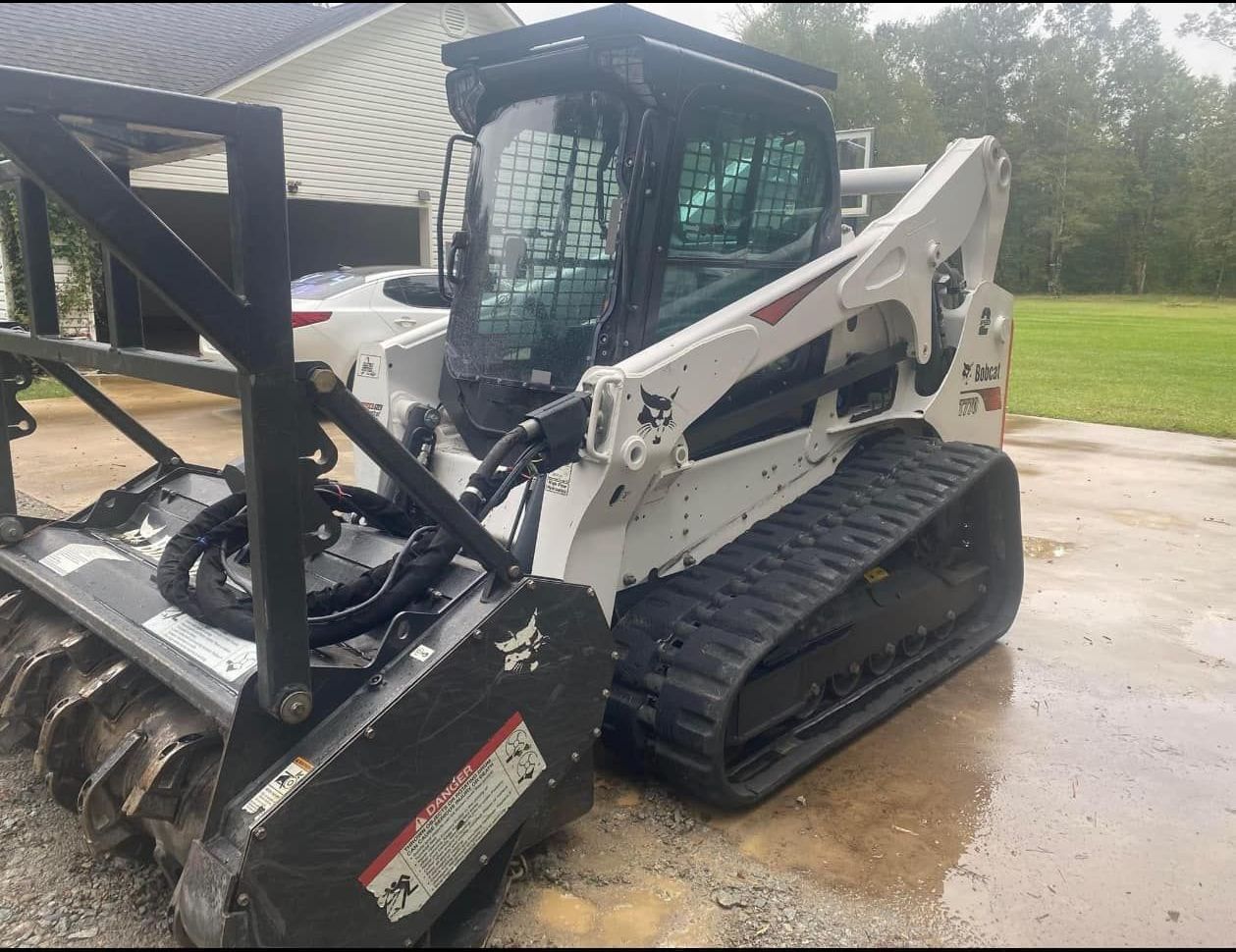 A bobcat is parked in a driveway next to a house.