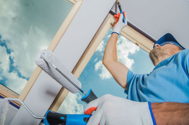 a man is painting the ceiling of a room with a roller