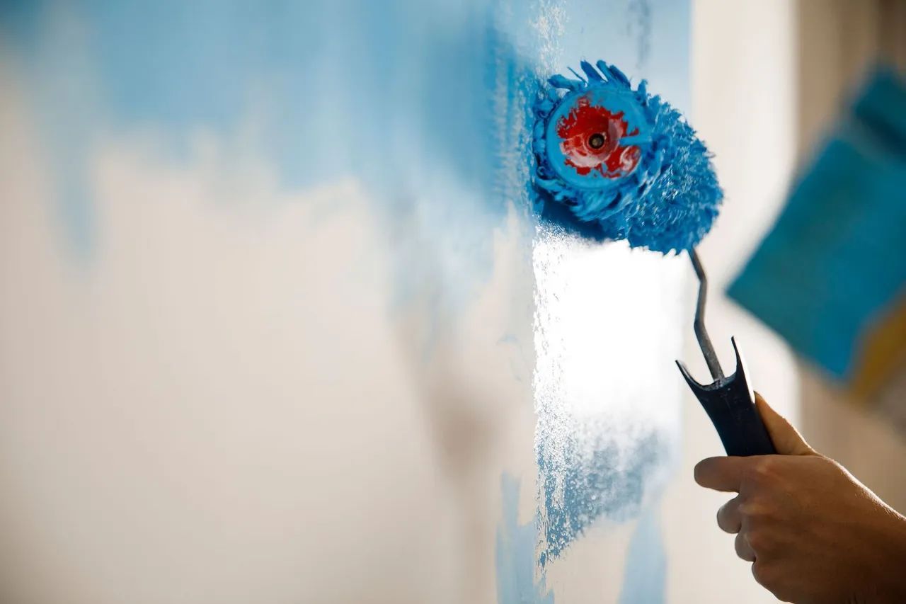 a person is painting a wall with a blue paint roller