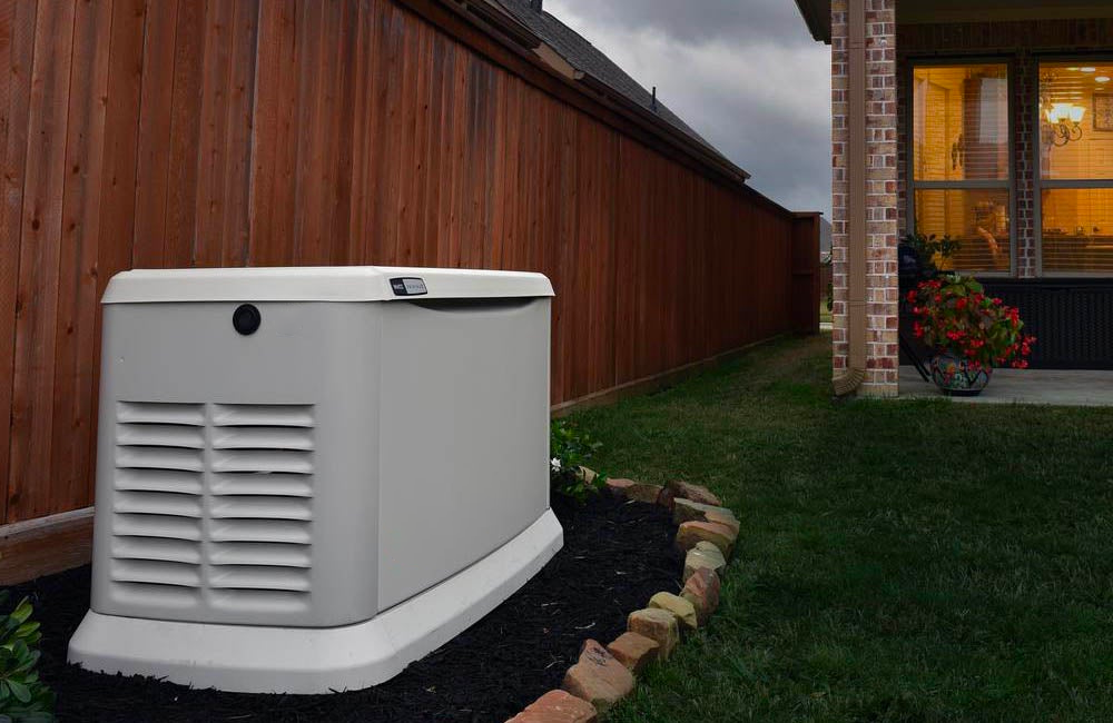 A generator is sitting in the backyard of a house next to a wooden fence.