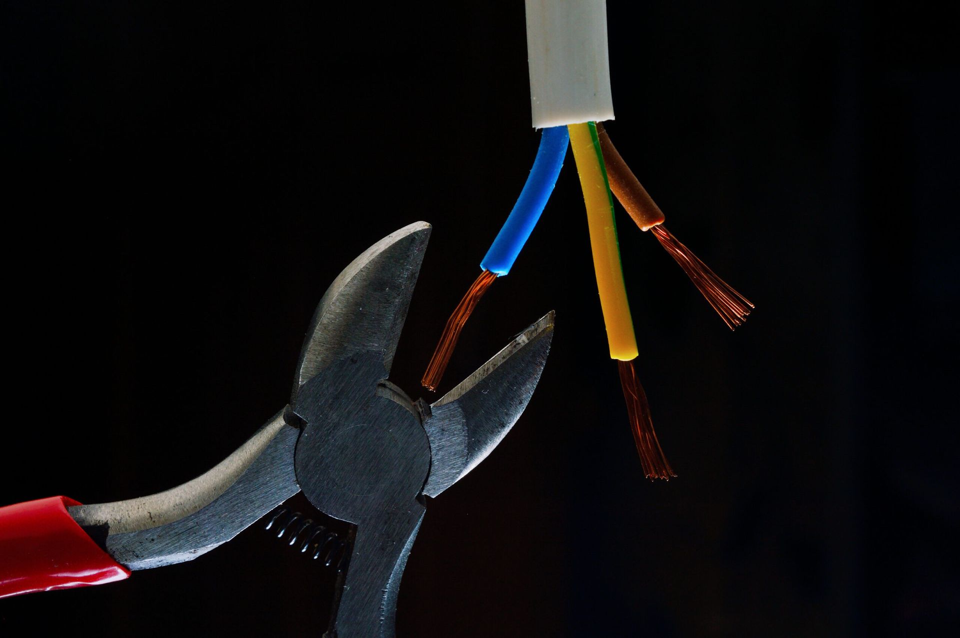 A pair of pliers is cutting a wire on a black background.