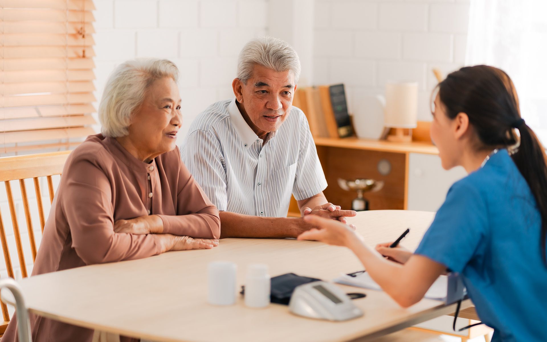 An elderly couple consults with a healthcare professional at a table indoors.