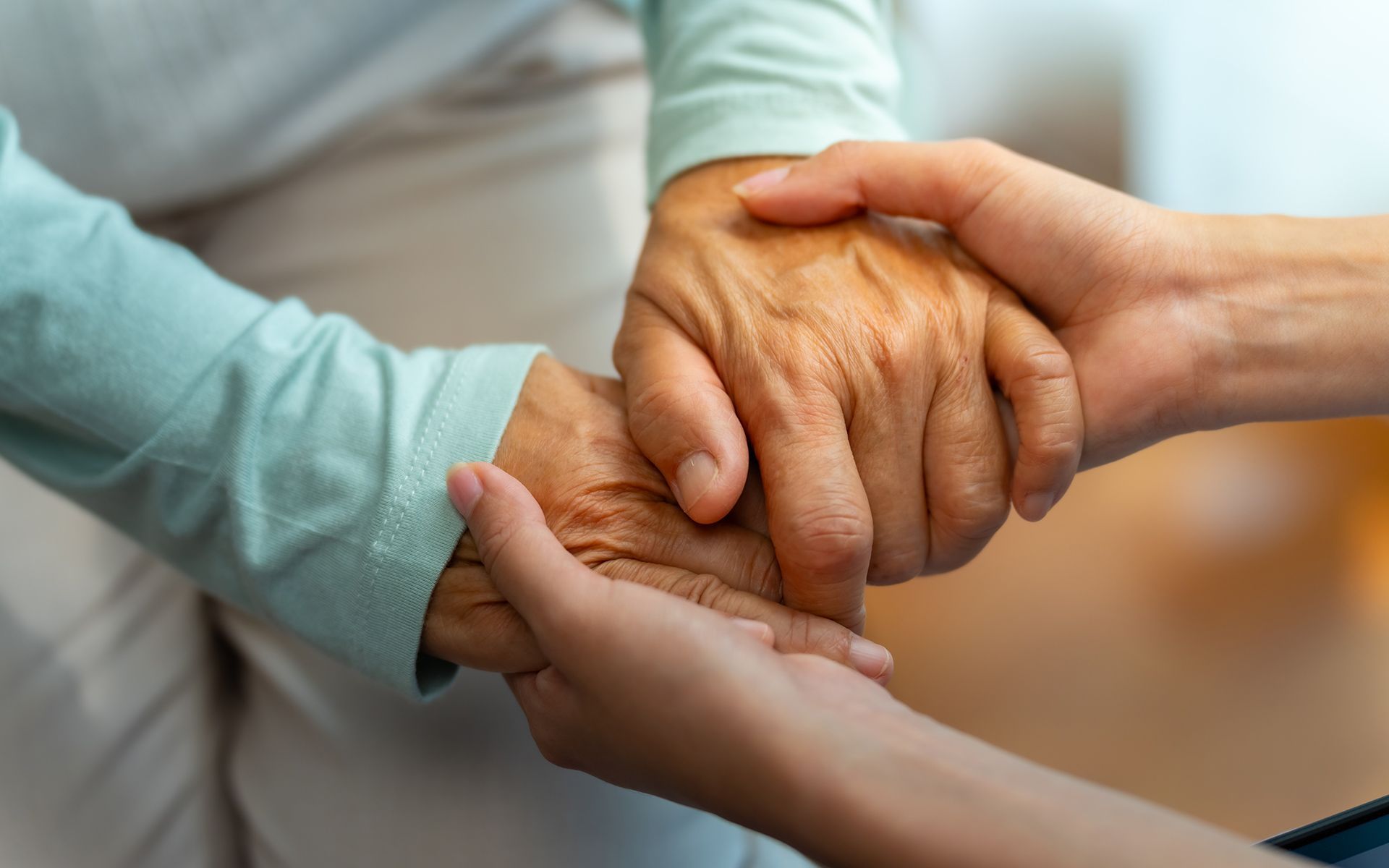 A young person's hands gently hold the wrinkled hands of an older person, offering support and comfort.