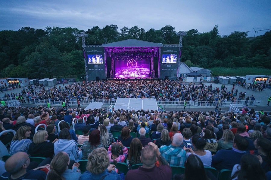 A crowd of people are sitting in front of a stage at a concert.