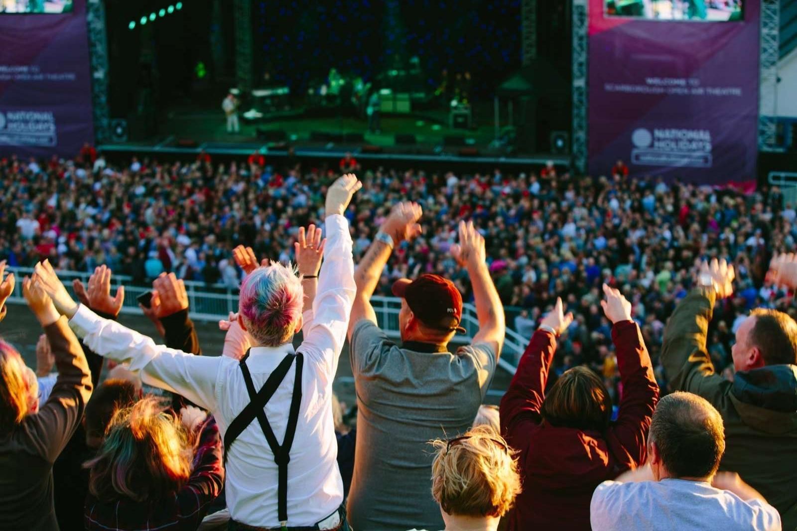 A crowd of people are watching a concert with their arms in the air.