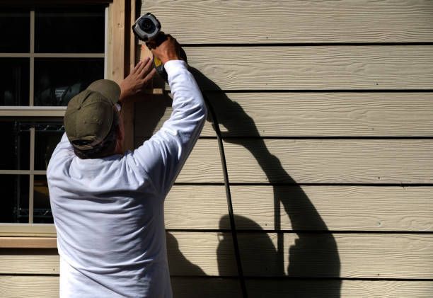 Person using a power tool to work on siding next to a window.