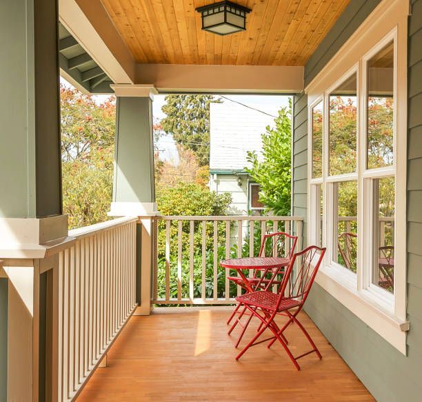 Cozy front porch with red table and chairs. Light wooden floor and ceiling, blue-green walls, white railing.