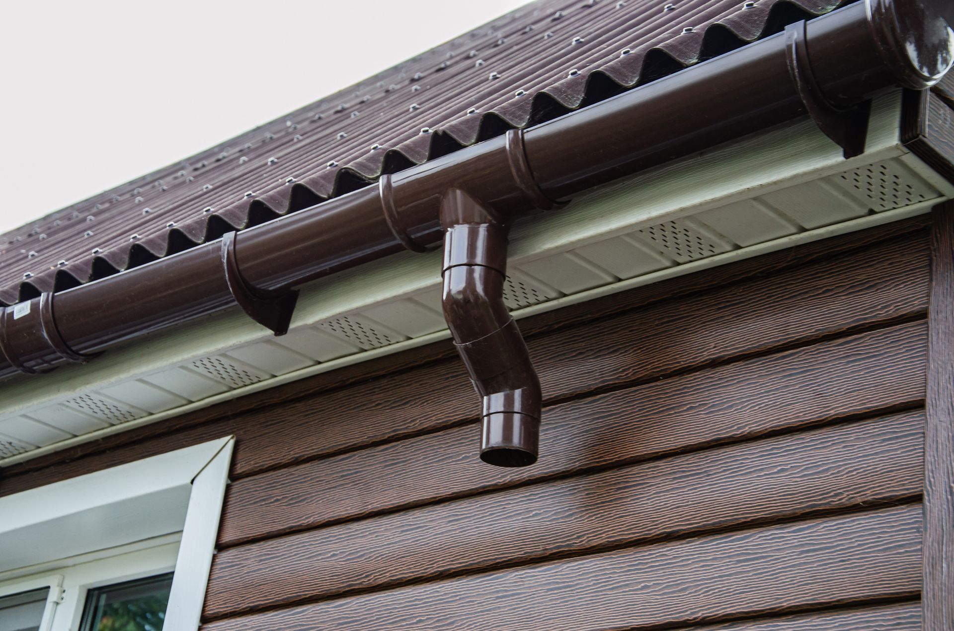 Brown gutters on a brown-sided house with a white trim and a brown roof.