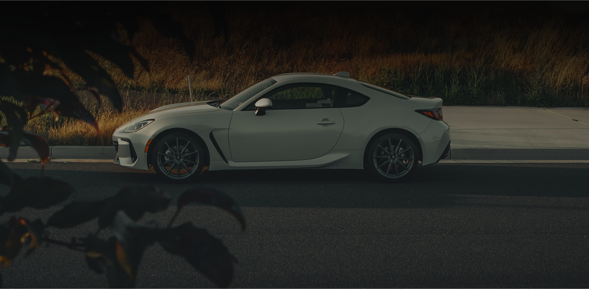 A white sports car drives on a road near foliage. | Deville Automotive