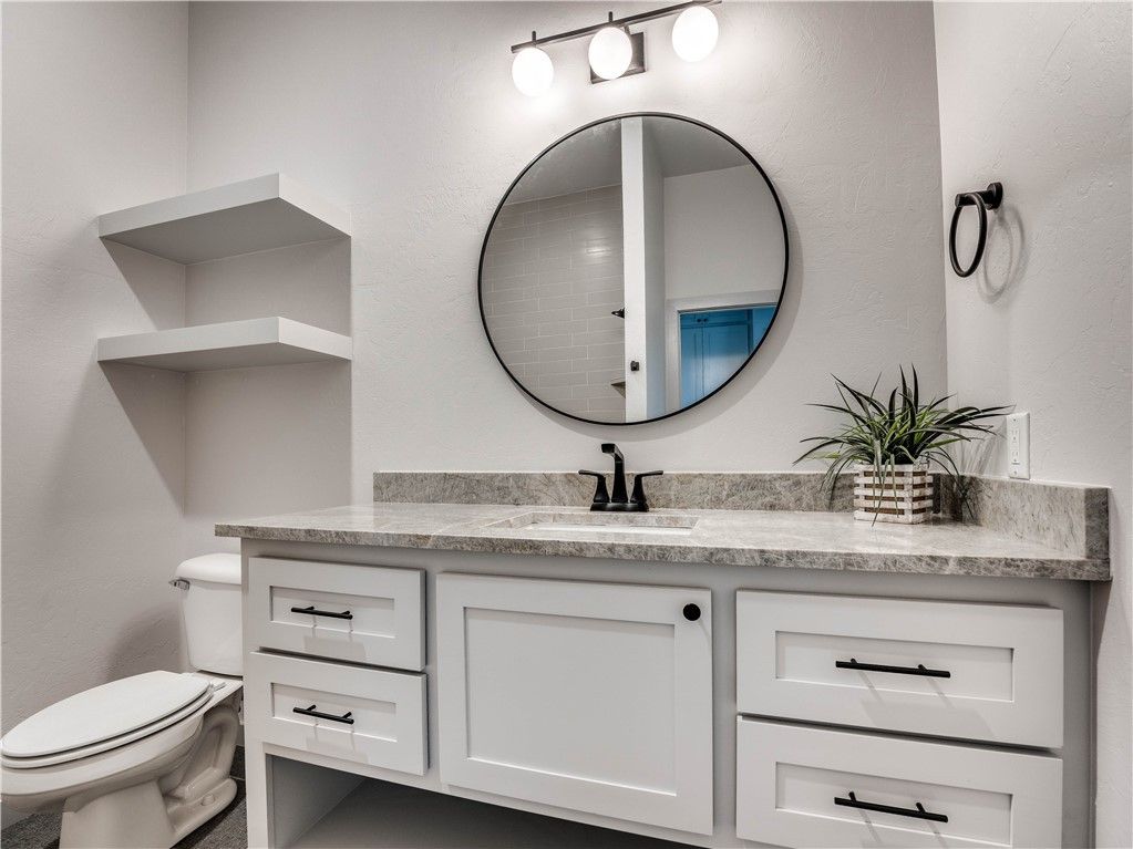 a bathroom with a toilet , sink , mirror and shelves