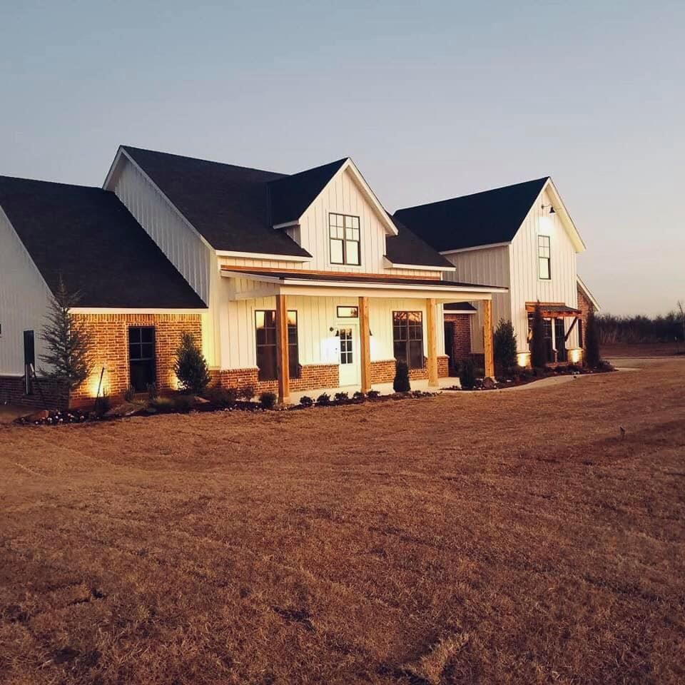 A large white house with a black roof is sitting in the middle of a field.