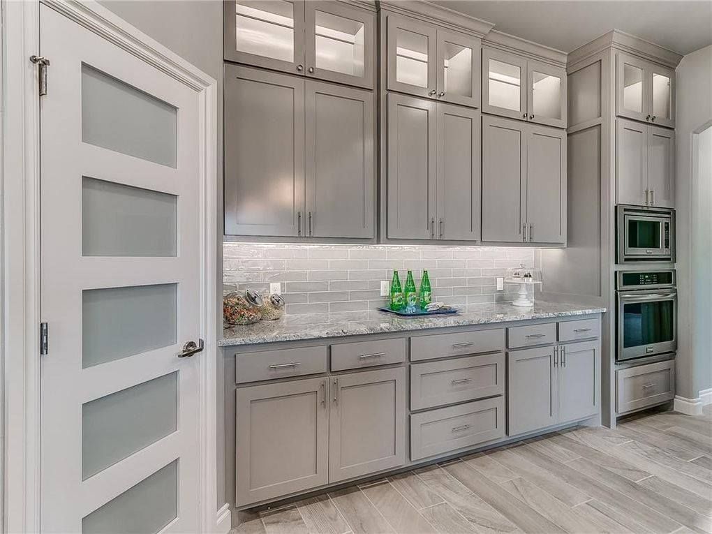 A kitchen with gray cabinets , granite counter tops , and stainless steel appliances.