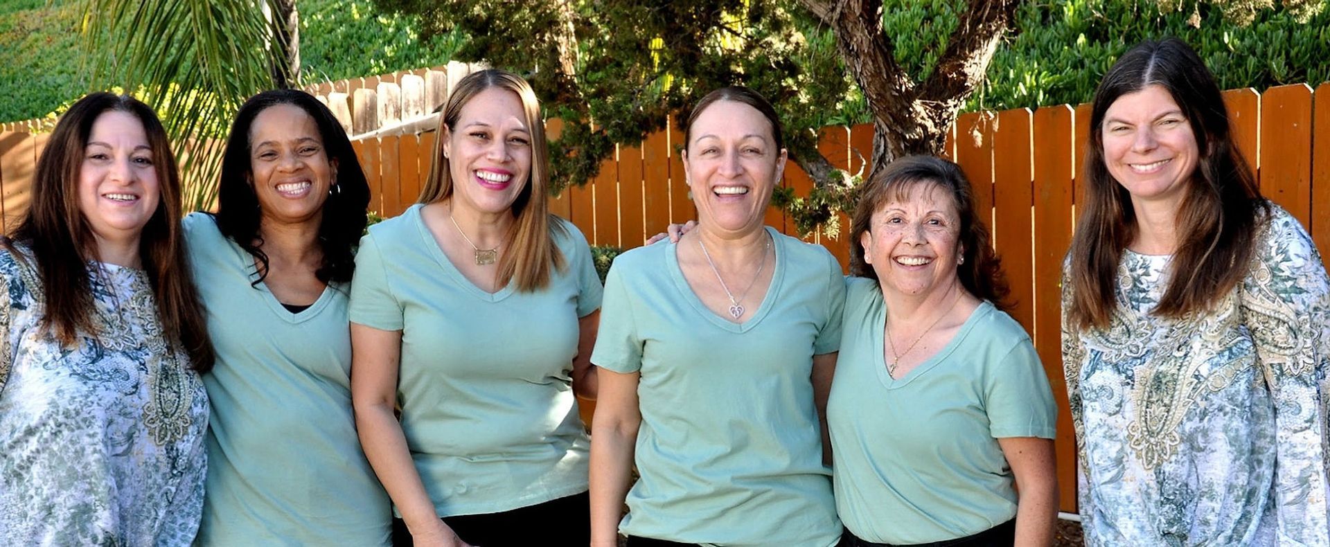 A group of women are posing for a picture in front of a wooden fence.
