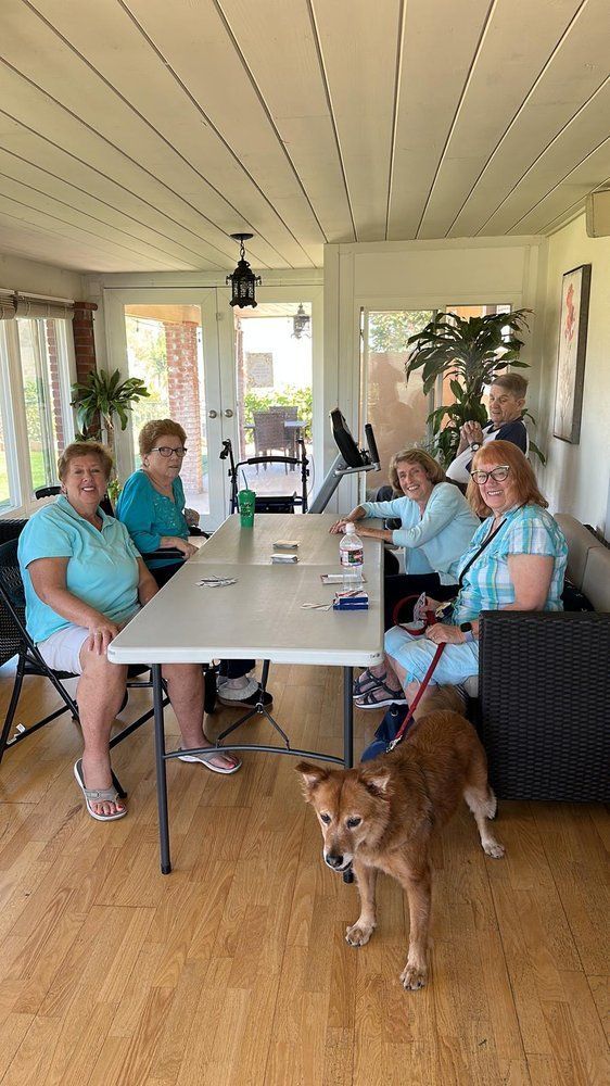 A group of people are sitting around a table with a dog standing next to them.