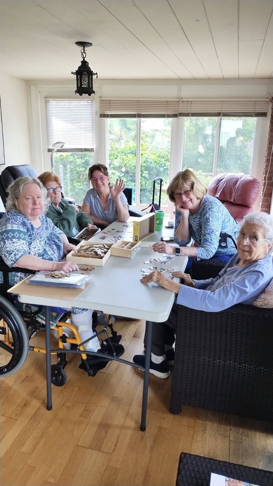 A group of elderly women are sitting around a table in a living room.